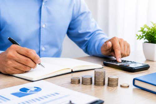 Pessoa a calcular despesas e prestações de crédito pessoal, com moedas, bloco de notas e calculadora sobre uma secretária.
